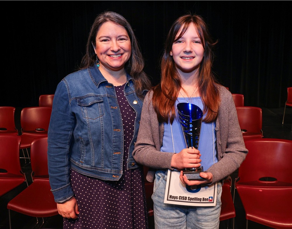 Hays CISD spelling bee representative standing next to an NES student carrying the 2nd place prize in the district spelling bee.