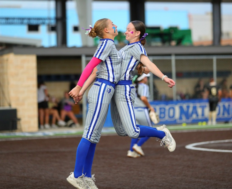 Two softball players chest bumping each other on the field.