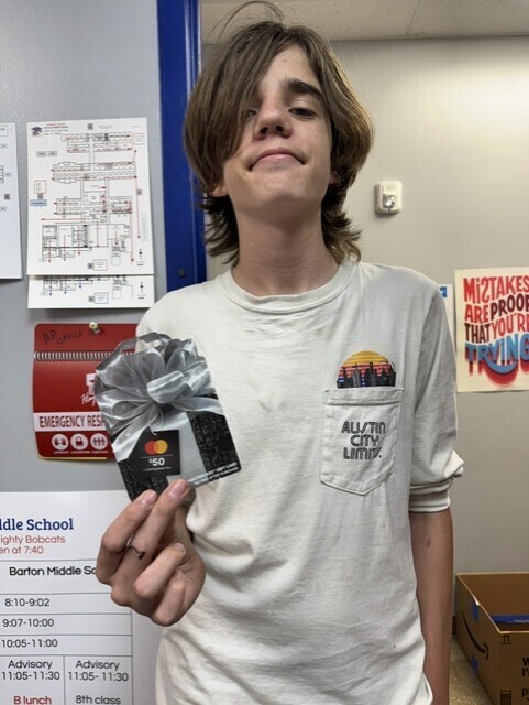 A young boy with long blonde hair holding a gift card