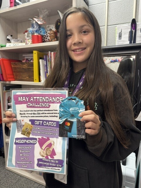A young girl with long brown hair carrying the May Attendance Challenge flyer and gift card.