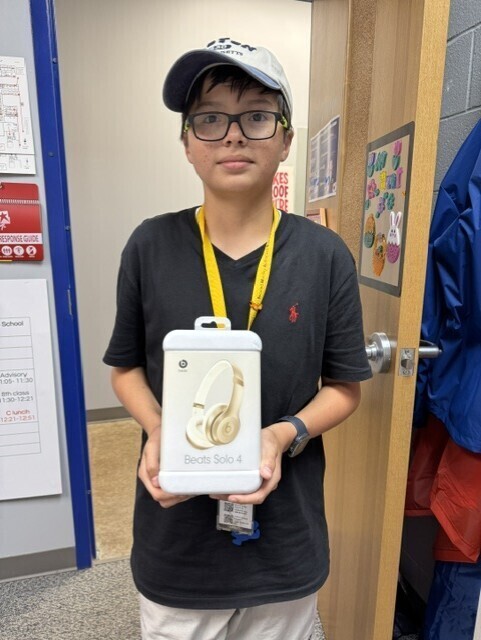 A young boy wearing a ball cap carrying new gold Beats headphones.