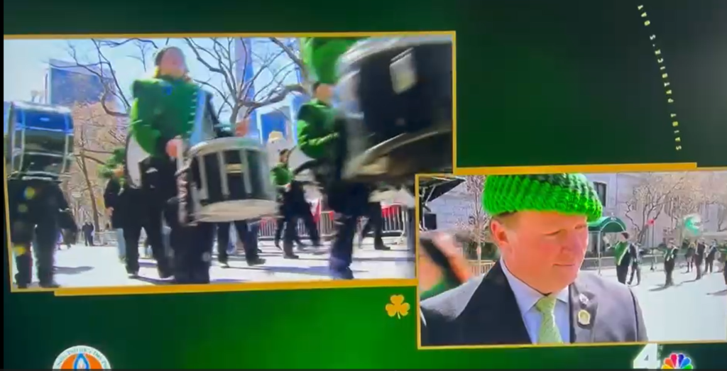 Picture of a news clip where the band is marching while someone is being interviewed.