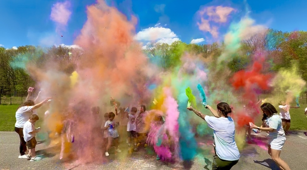 Students participating in a color run.  multiple colors are being splashed onto a groujp of students and teachers. 