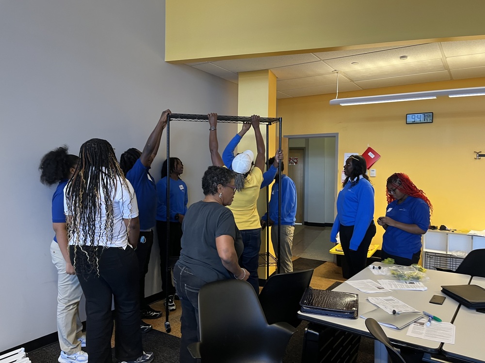 A group of people wearing blue shirts gathered around a tall metal frame structure during an activity in a classroom setting.