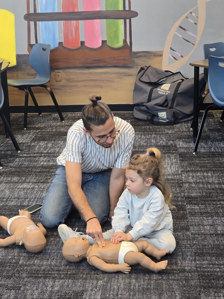 A man and his daughter doing CPR to a baby dummy