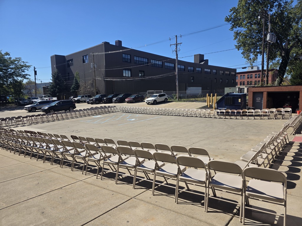 A bunch of empty folding chairs in the parking lot arranged in a square.