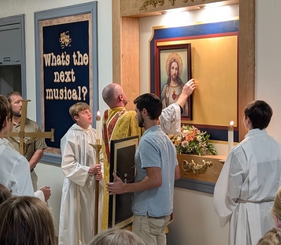 Fr. Brian hangs the image of the Sacred Heart of Jesus in the hallway at TMP-Marian