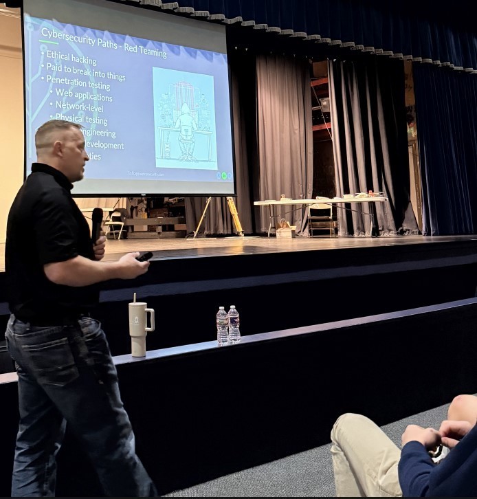 A man in a black shirt presents a slide to students