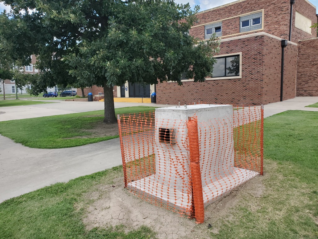 Concrete foundation for new bison statue surrounded by orange construction fencing.