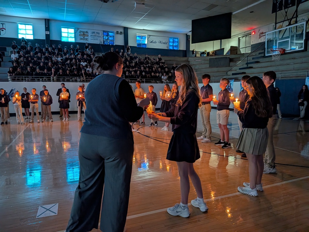 A female student lights a candle held by a teacher.