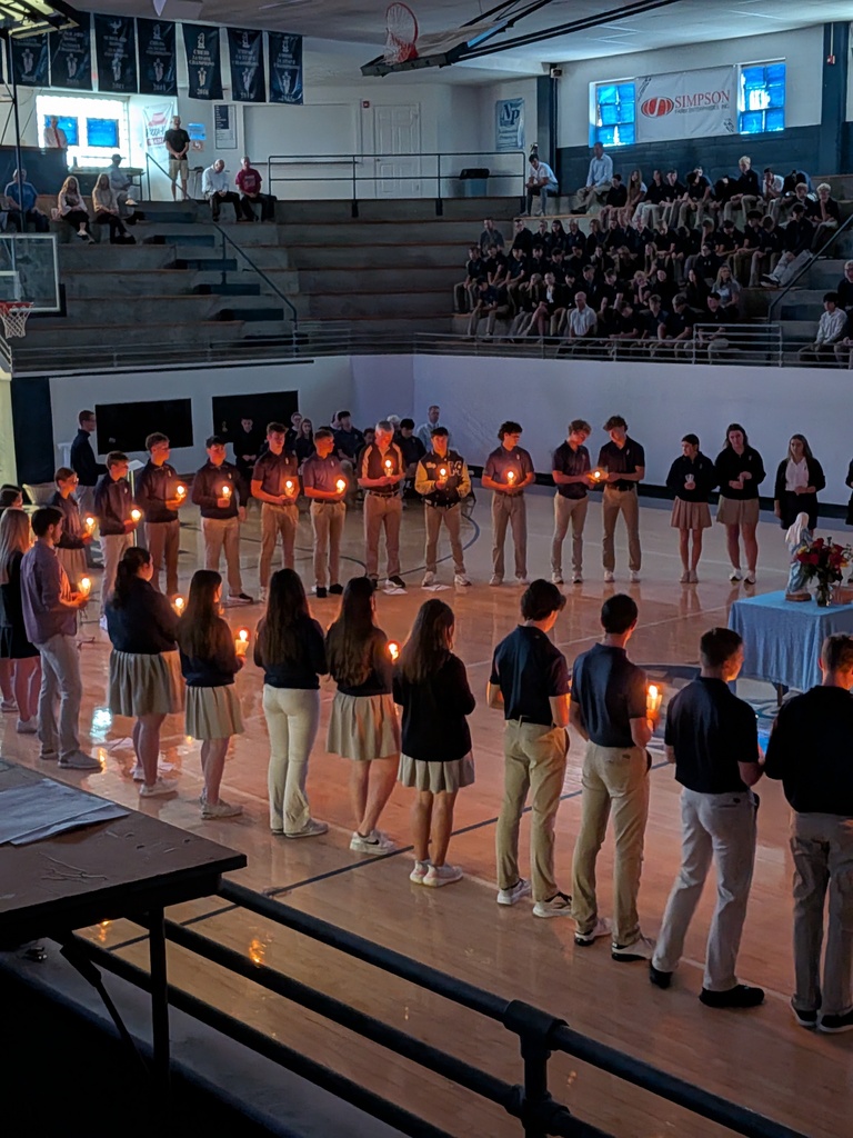 Students on a gym floor hold candles to represent each prayer