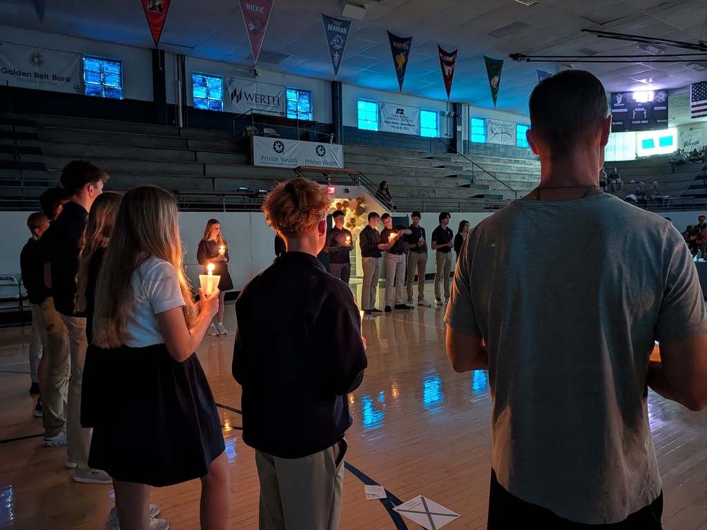 Students and teacher stand with candles during a living rosary.