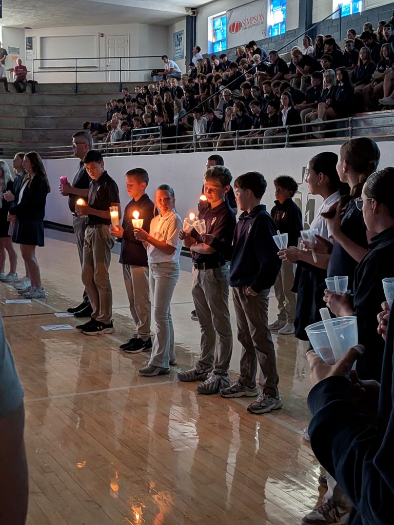 Junior high students stand in a circle lighting a candle.