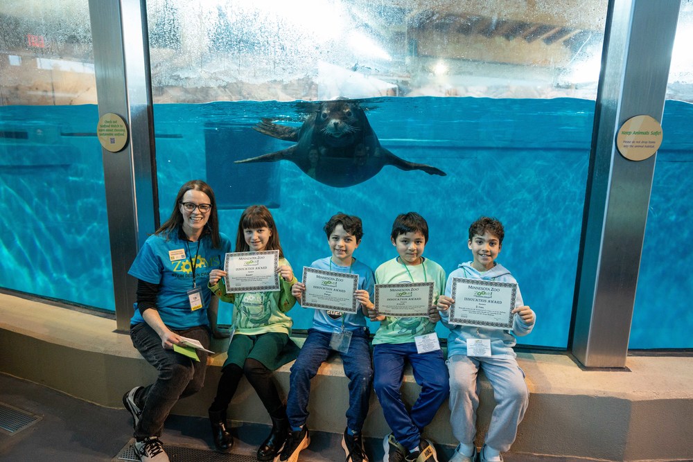 third graders hold first place ZOOMS certificates, posed in front of sea lion
