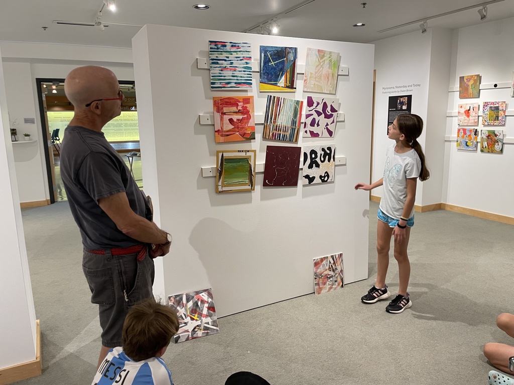 student examines abstract square paintings on wall. 9 paintings in 3 rows of 3