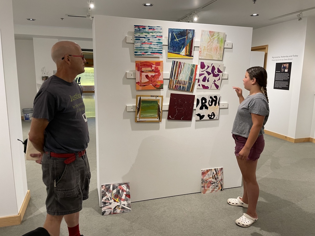 student examines abstract square paintings on wall. 9 paintings in 3 rows of 3