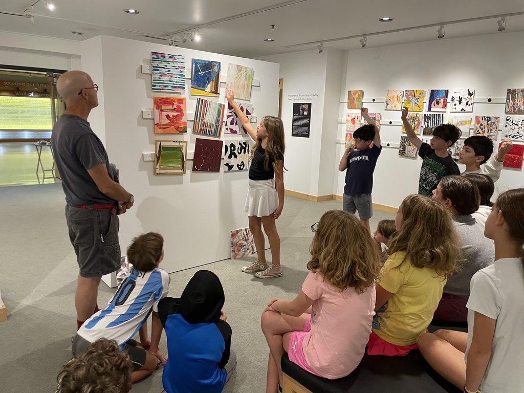 student points to painting on wall as others watch some raising hands