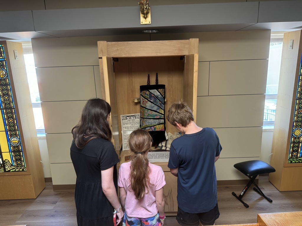 two students and volunteer look at question printed in front of torah in ark