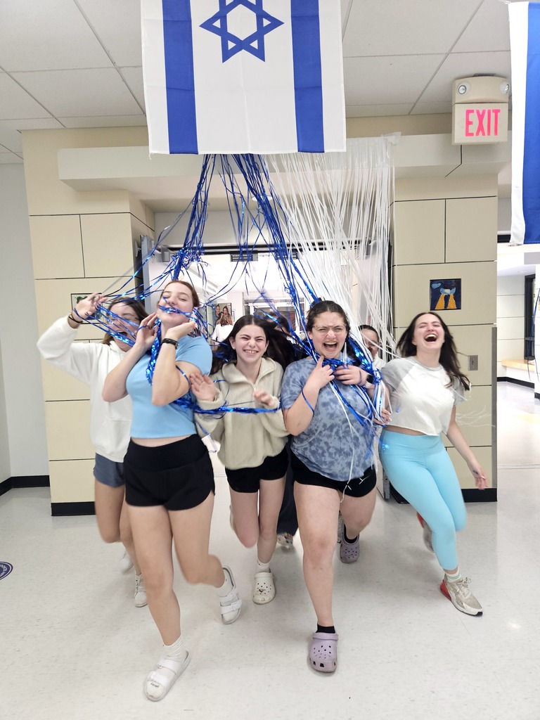 smiling students walk through blue and white streamers  under Israeli flag