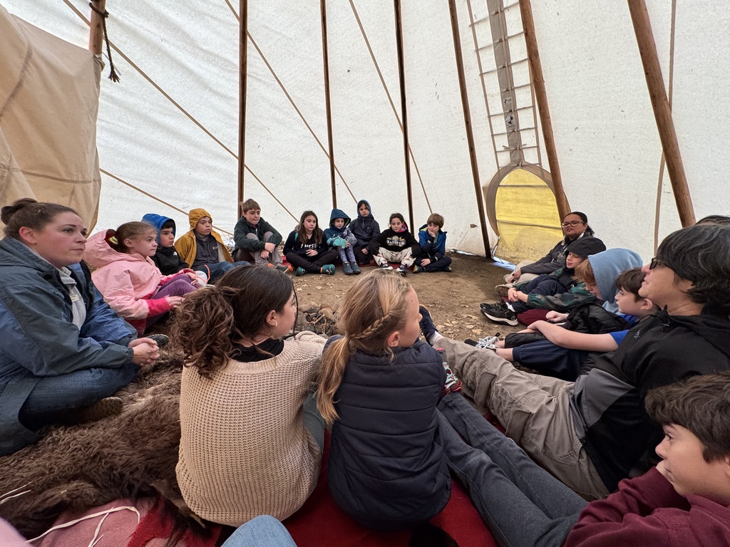 students sit in circle inside tipi