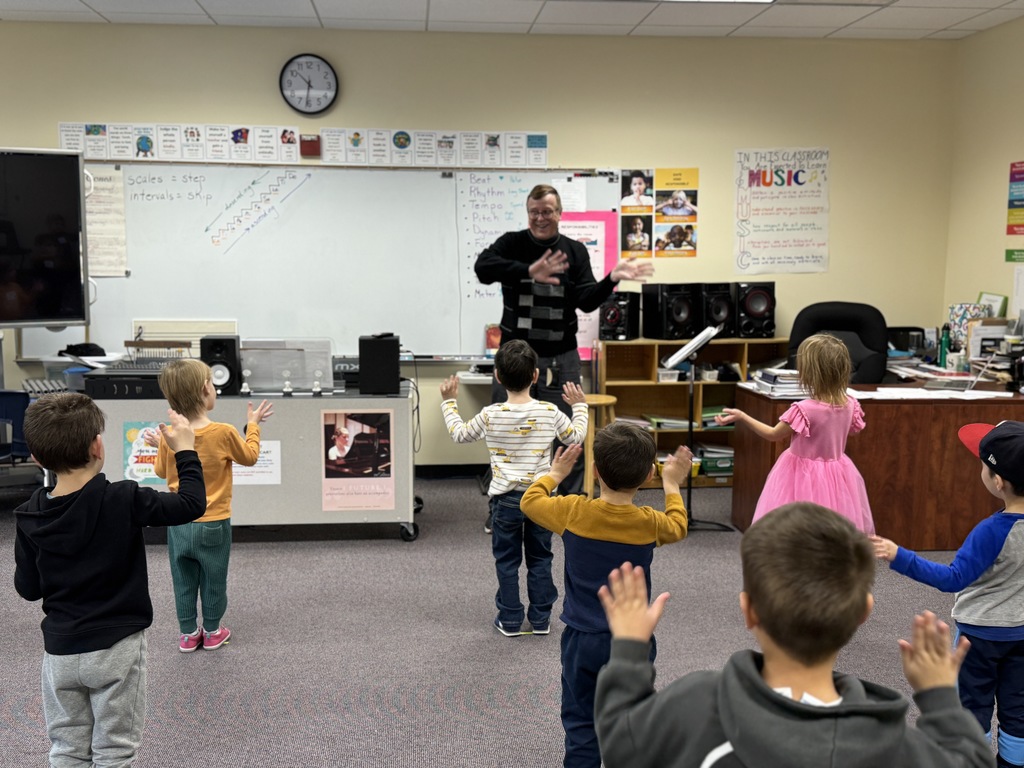 pre-k students wave arms, following music teacher's lead