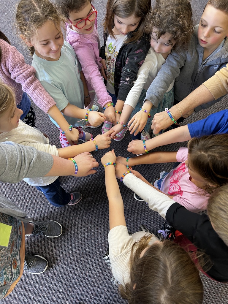 K students and teachers put there hands together, showing family bracelets on their wrists