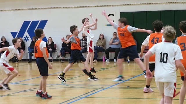 opposing basketball player shoots ball as Heilicher players attempt block