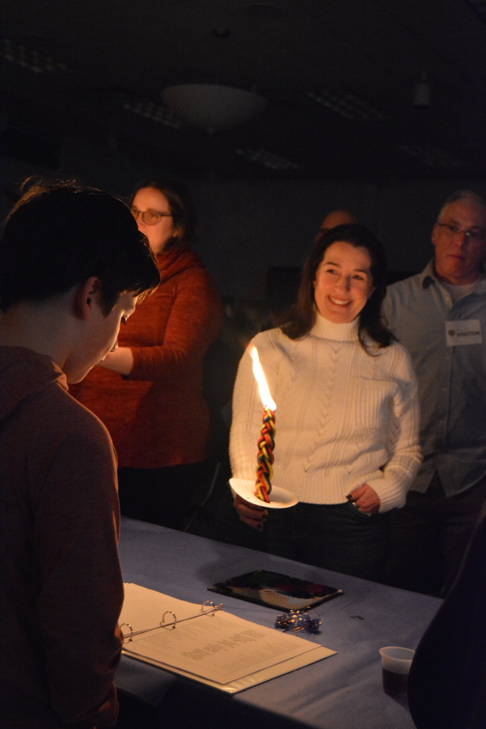 student sings blessings as his mom holds Havdalah candle