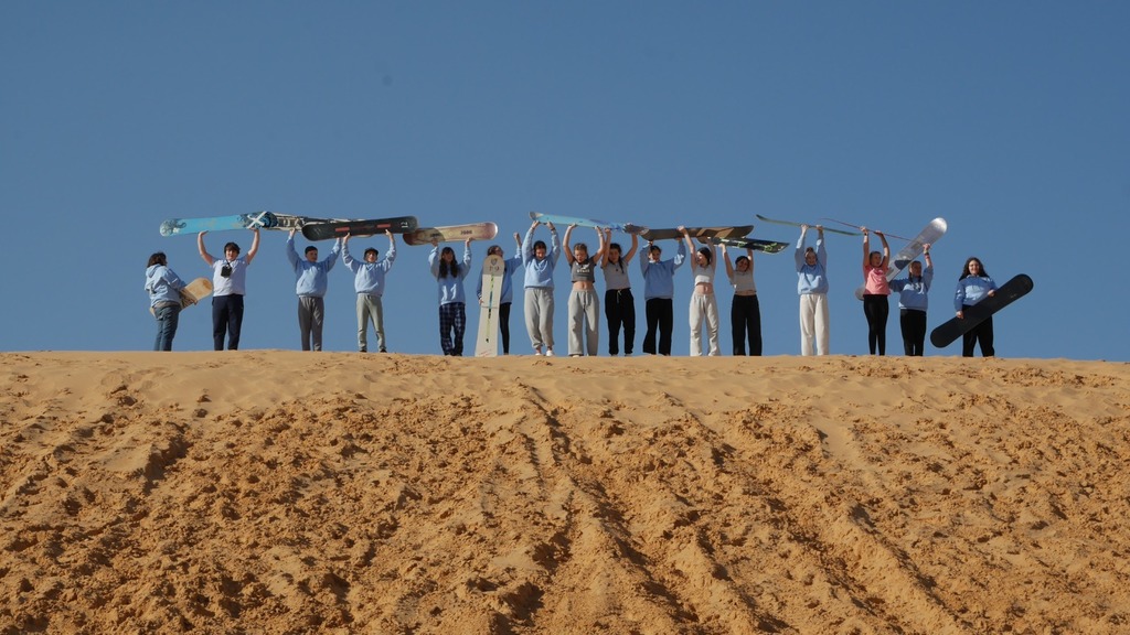 students  raise sandboards above their heads on top of dune