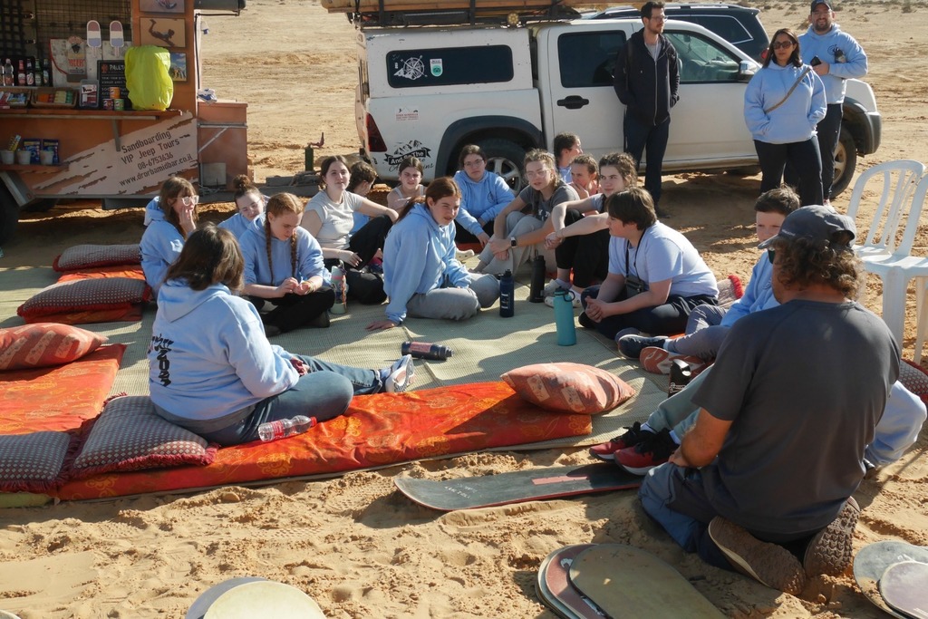 students sit on a mat in the sand