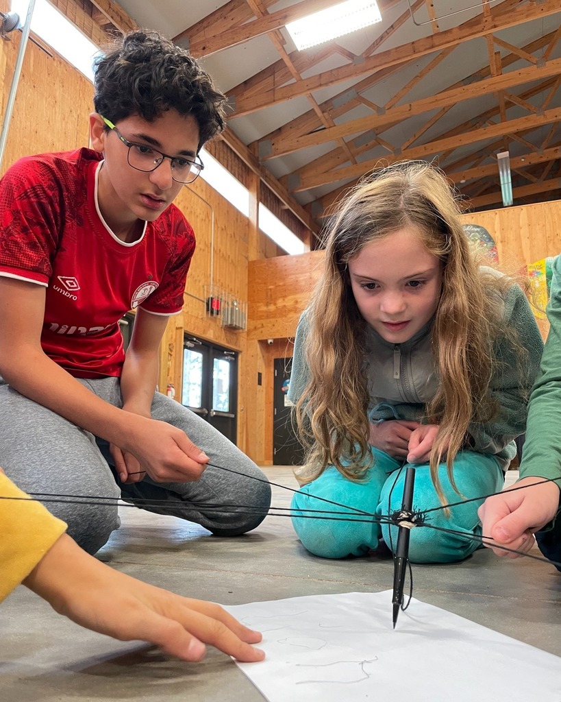 students work together to control pen with strings