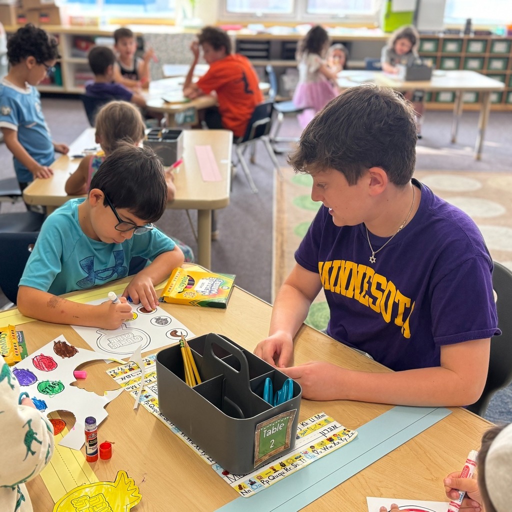 kindergartner colors Rosh Hashanah crown with eighth grade buddy