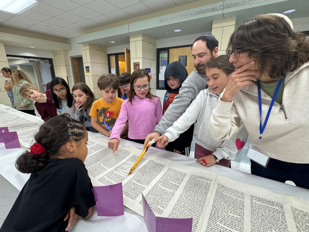 Rabbi points to a section in a rolled out Torah as students look on on Simchat Torah
