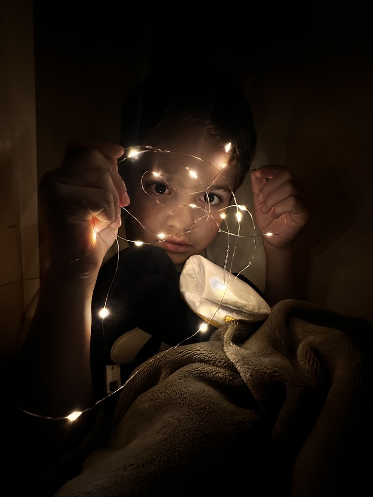 girl in the dark holds glowing string lights in front of her face