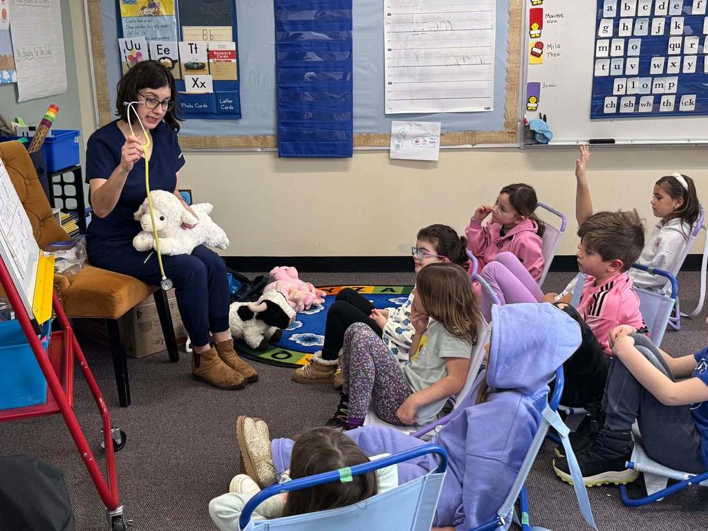 Vet shows stethoscope to first graders, one student raises hand