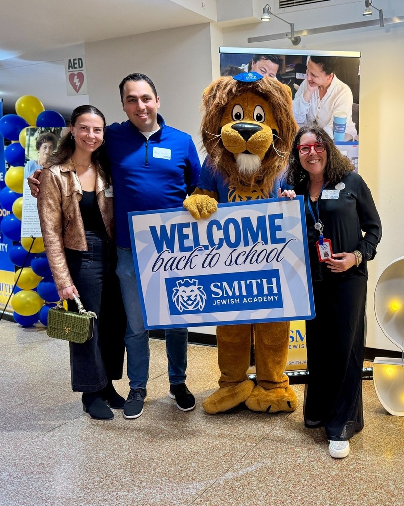 guests pose with Roary the Lion mascot and welcome back to school sign