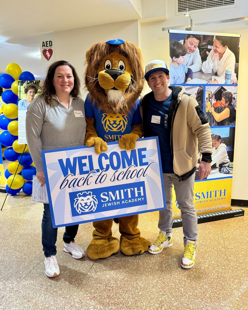guests pose with Roary the Lion mascot and welcome back to school sign