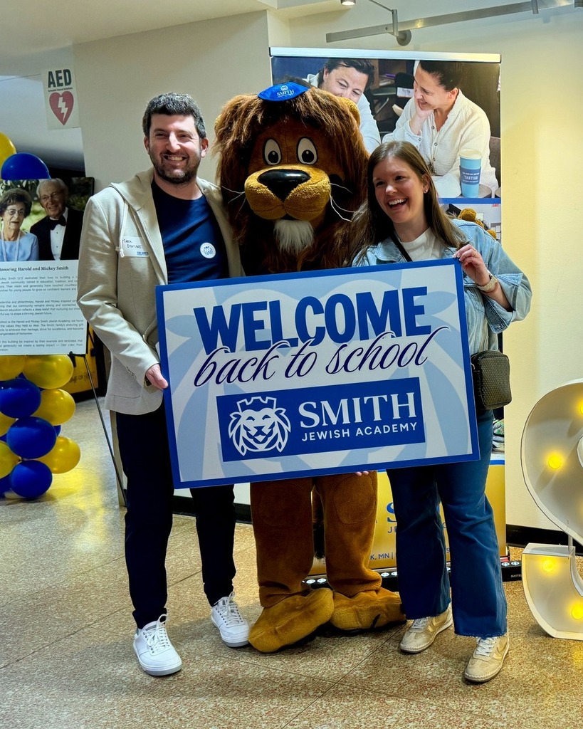 guests pose with Roary the Lion mascot and welcome back to school sign