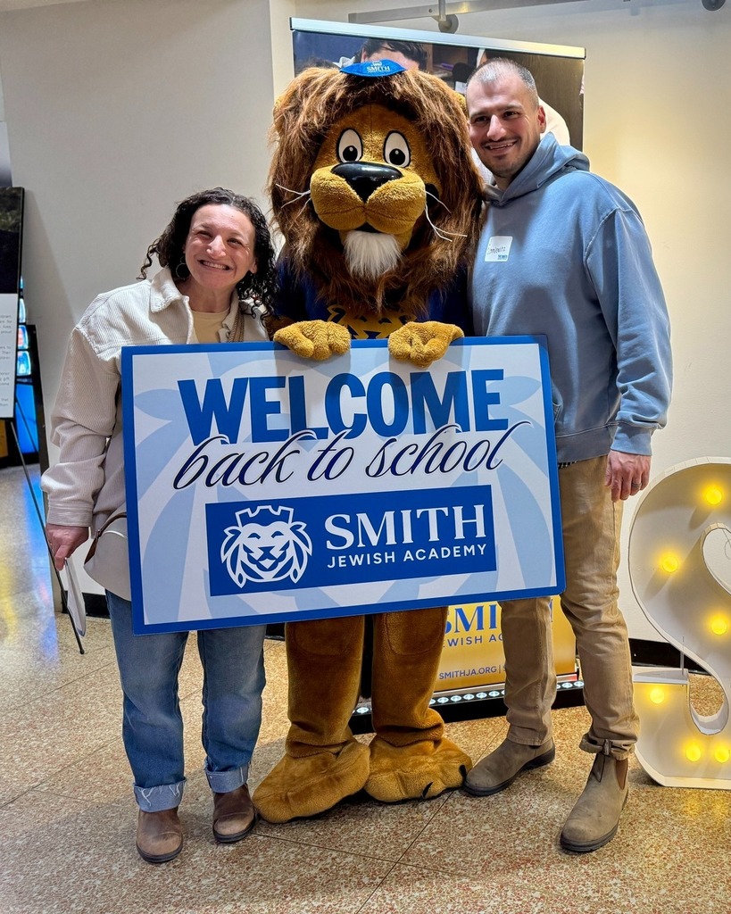 guests pose with Roary the Lion mascot and welcome back to school sign