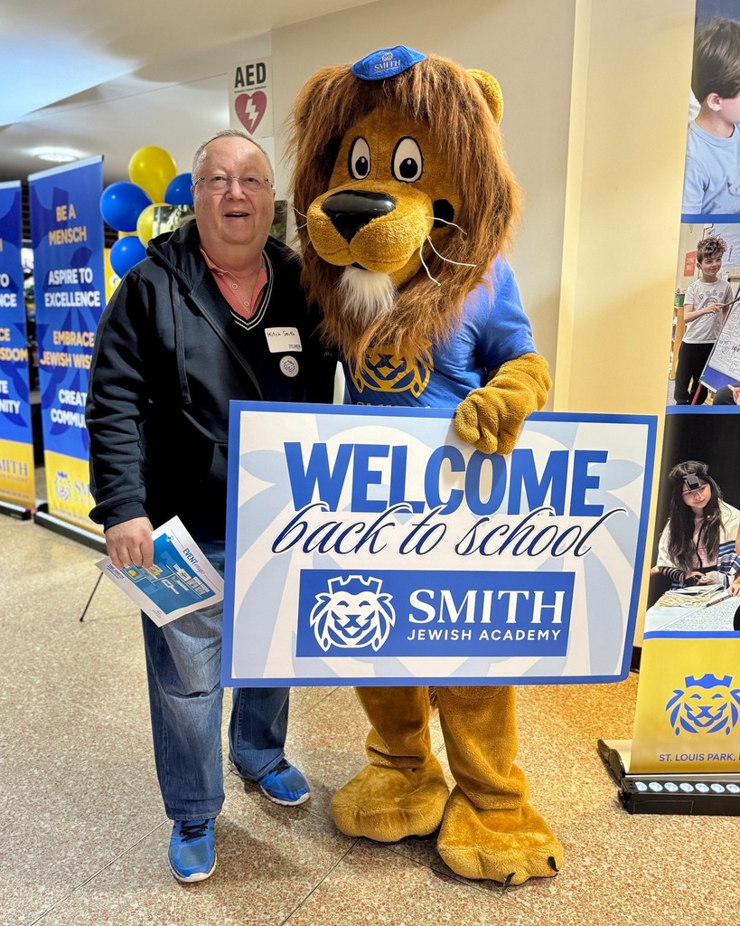 guests pose with Roary the Lion mascot and welcome back to school sign