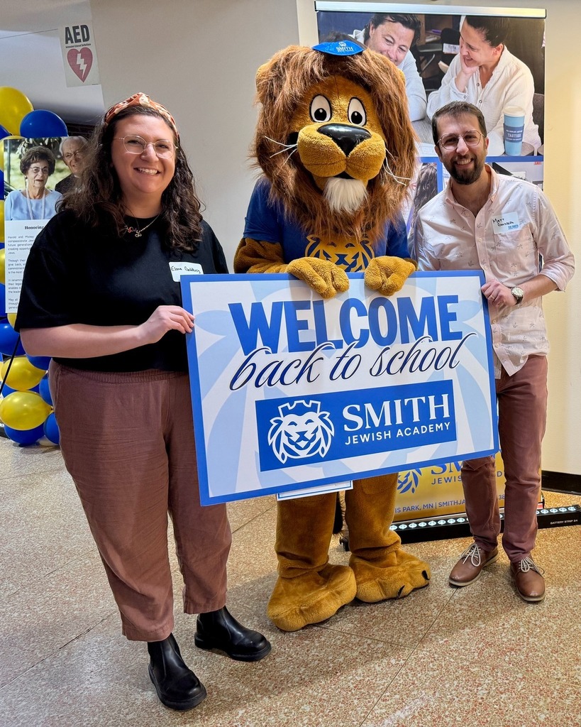 guests pose with Roary the Lion mascot and welcome back to school sign