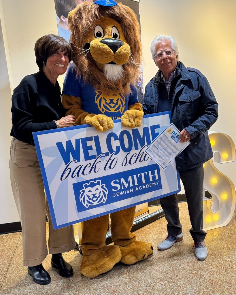 guests pose with Roary the Lion mascot and welcome back to school sign