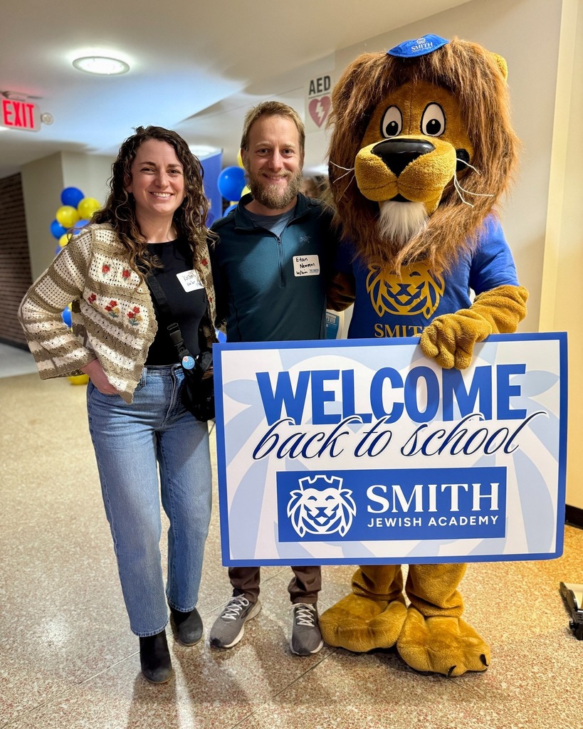 guests pose with Roary the Lion mascot and welcome back to school sign