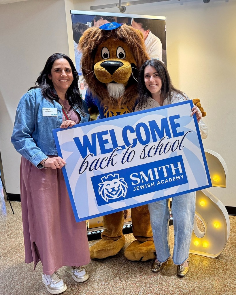 guests pose with Roary the Lion mascot and welcome back to school sign