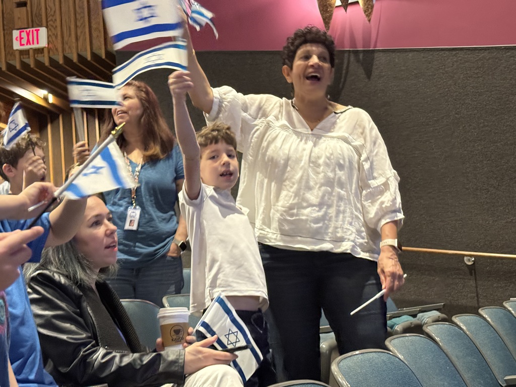 students and teachers sing and wave Israeli flags