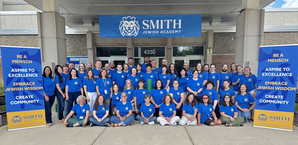 full staff photo, everyone in blue shirts with SJA lion logo. SJA banners