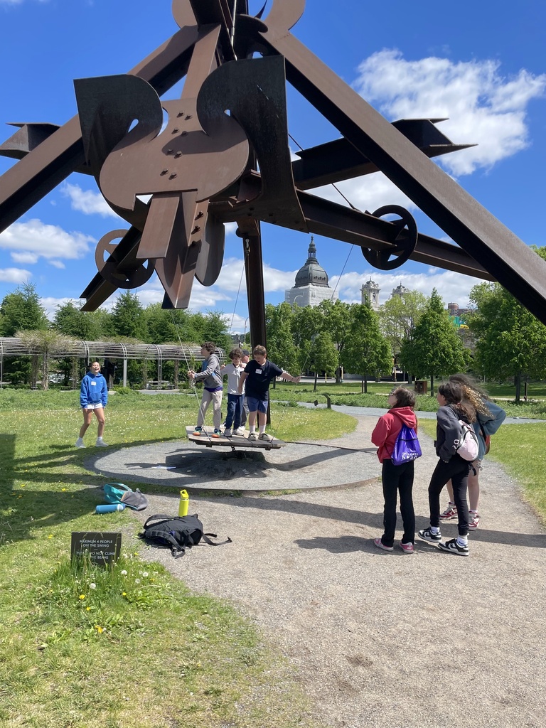 fifth graders stand on Arikidea swing sculpture