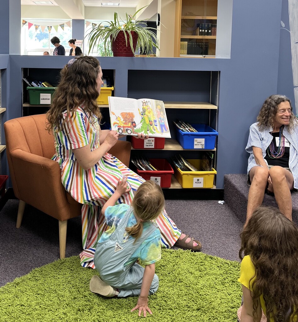 woman in vertical rainbow striped dress reads story book to children and adults