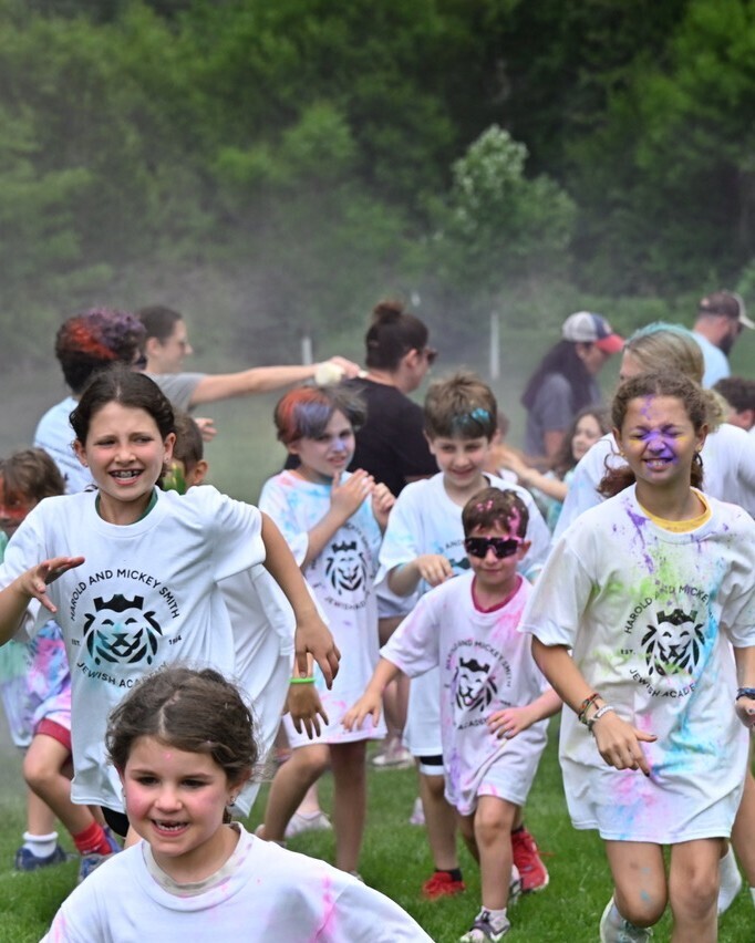 students covered in colorful chalk run through chalk tossed by parents
