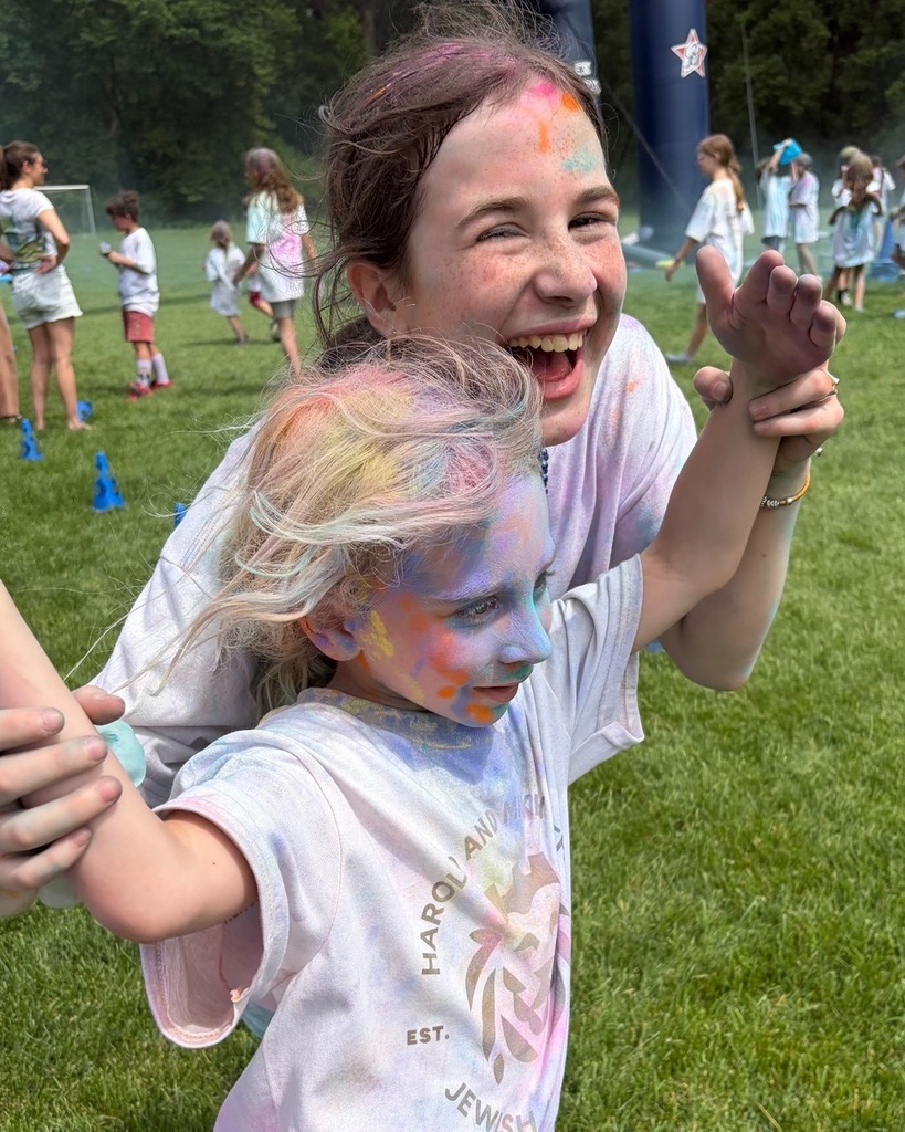 older student and younger student run together covered in colorful chalk